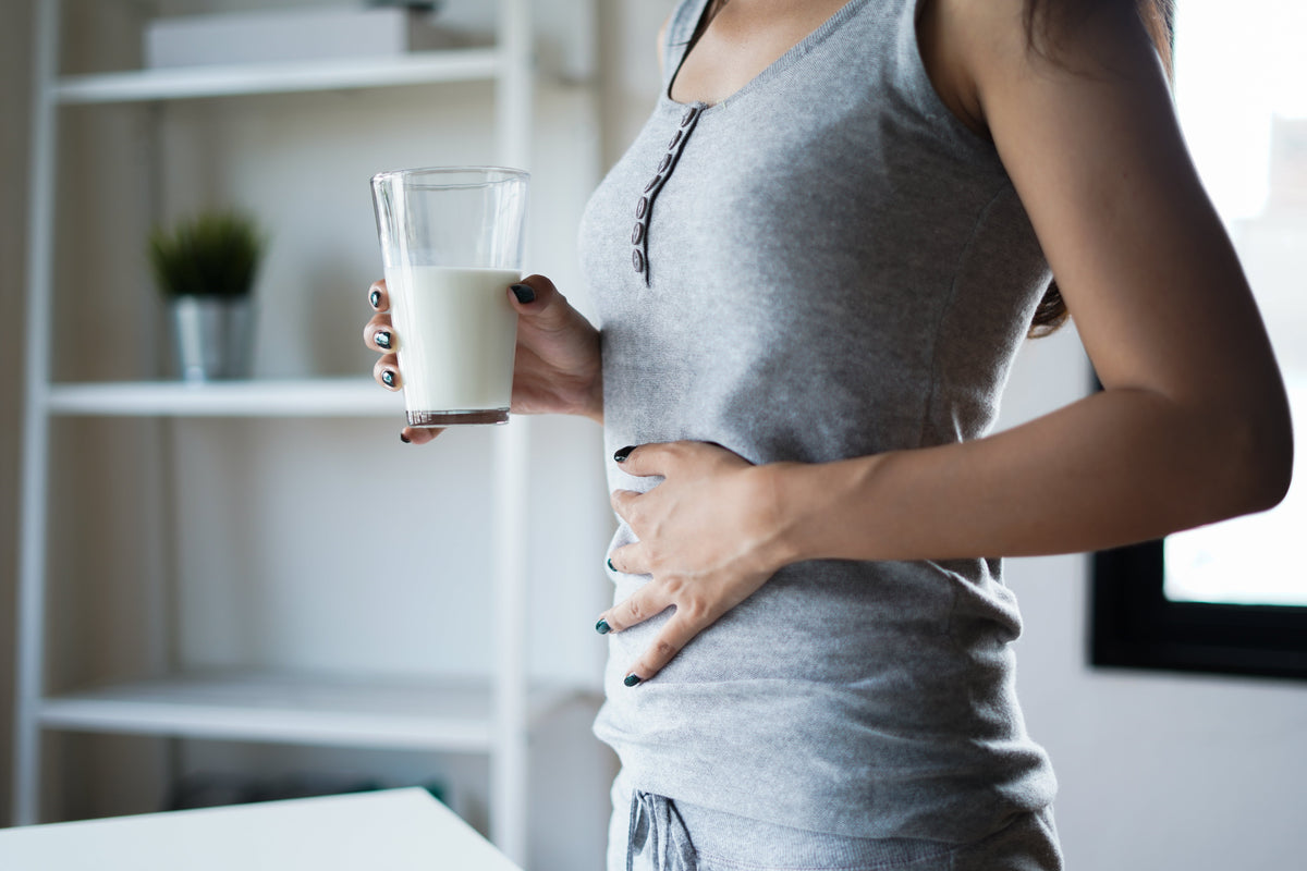 Mujer cogiendo un vaso de leche y tocándose la barriga
